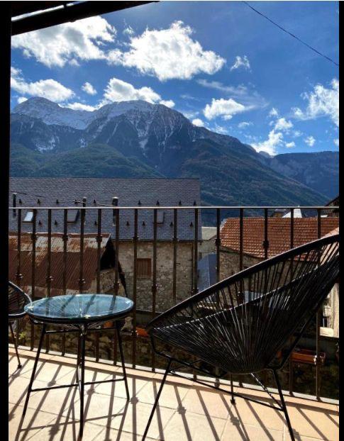 Balcón con vista a montañas nevadas, decorado con sillas de diseño moderno y una mesa de cristal, bajo un cielo azul con nubes. Ideal para disfrutar de la naturaleza y la tranquilidad.