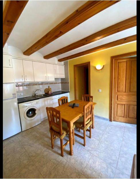 Cocina acogedora con mesa de comedor de madera y sillas, electrodomésticos modernos, y paredes de color amarillo. Ideal para comidas familiares y momentos de convivencia.