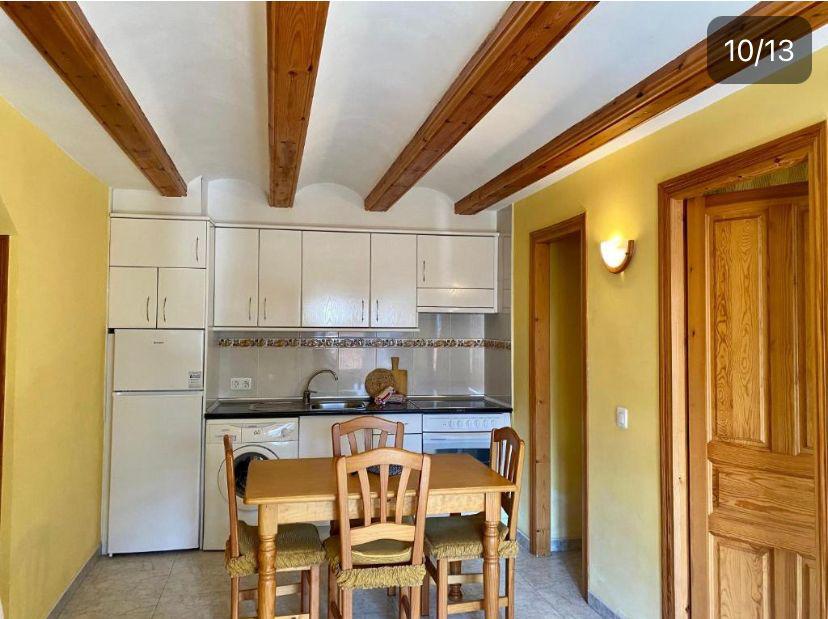 Cocina moderna y acogedora con muebles de madera, mesa y sillas, electrodomésticos blancos, y paredes amarillas, ideal para un ambiente familiar.