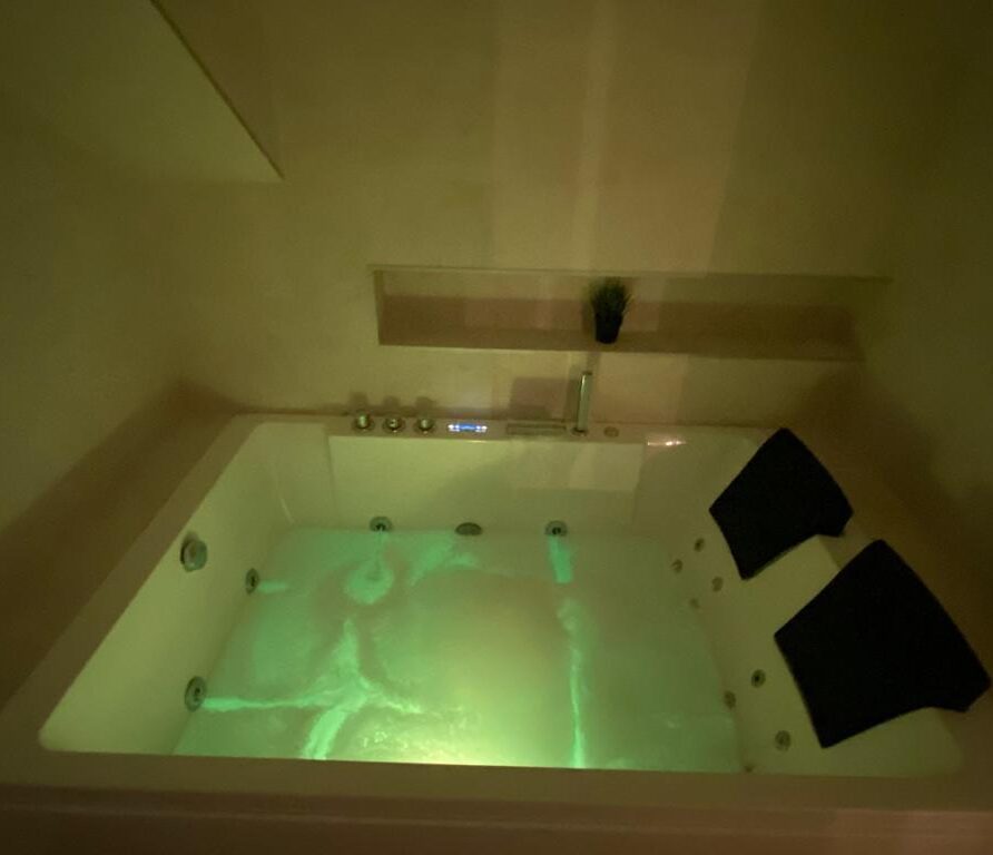 Jacuzzi moderno iluminado con luz verde, equipado con asientos y rodeado de un ambiente relajante. Ideal para momentos de bienestar y spa en casa.
