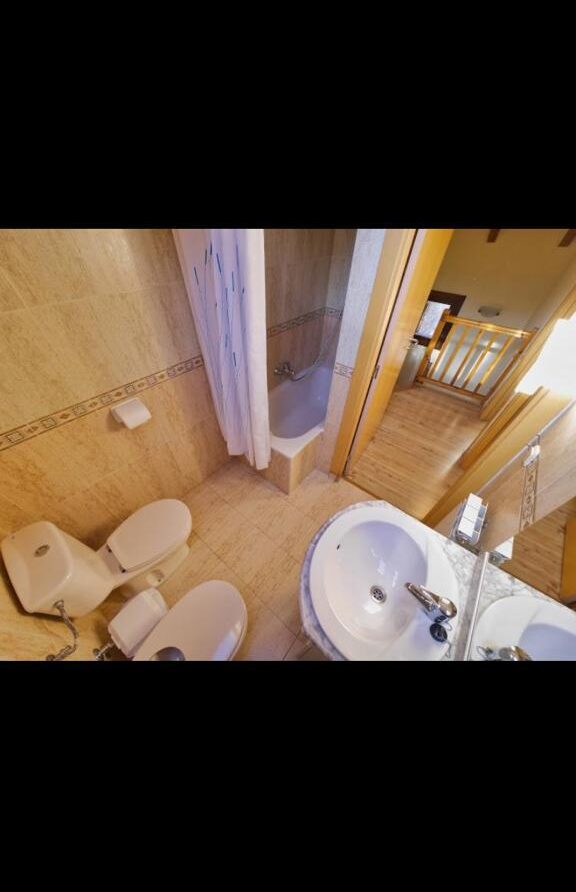 Baño moderno con ducha, inodoro y lavabo, decorado con azulejos claros y suelo de madera. Ideal para un ambiente acogedor y funcional.