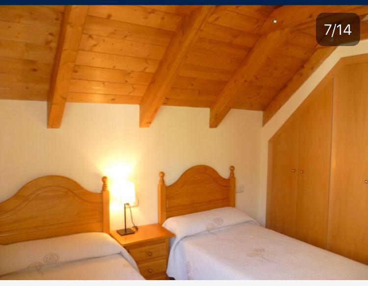 Habitación acogedora con dos camas individuales, lámpara de mesa y armario empotrado, decorada con techos de madera y paredes claras. Ideal para un descanso tranquilo.